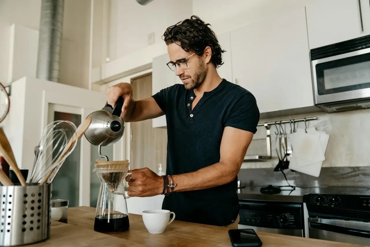A man pouring hot water over coffee in his kitchen