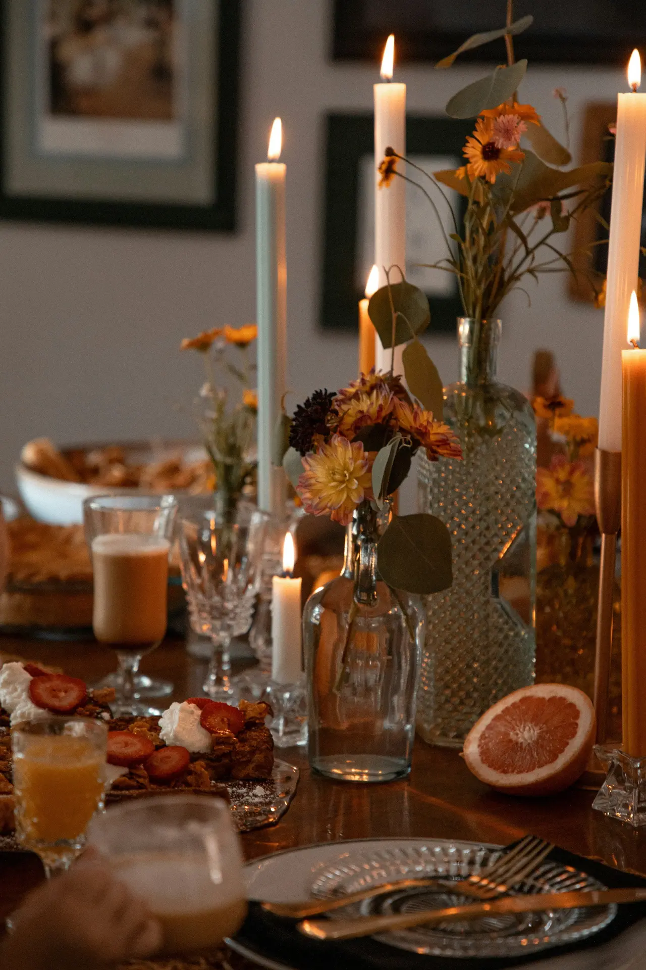 A candlelit dinner table set with oranges and greenery