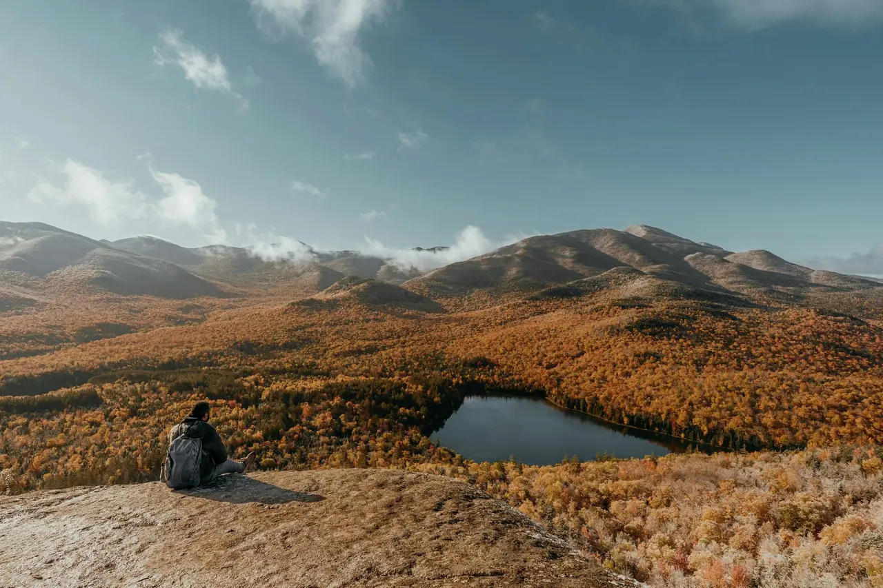 A hiker resting on a rock above a lake in golden hills