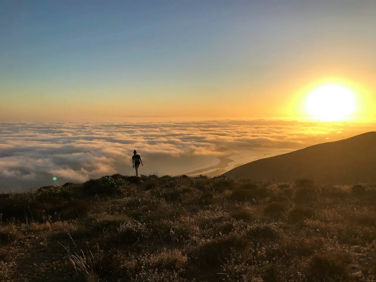 A hiker on a ridge above a sea of clouds at sunset