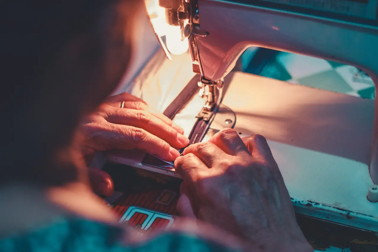 Hands guiding fabric through a sewing machine in warm light