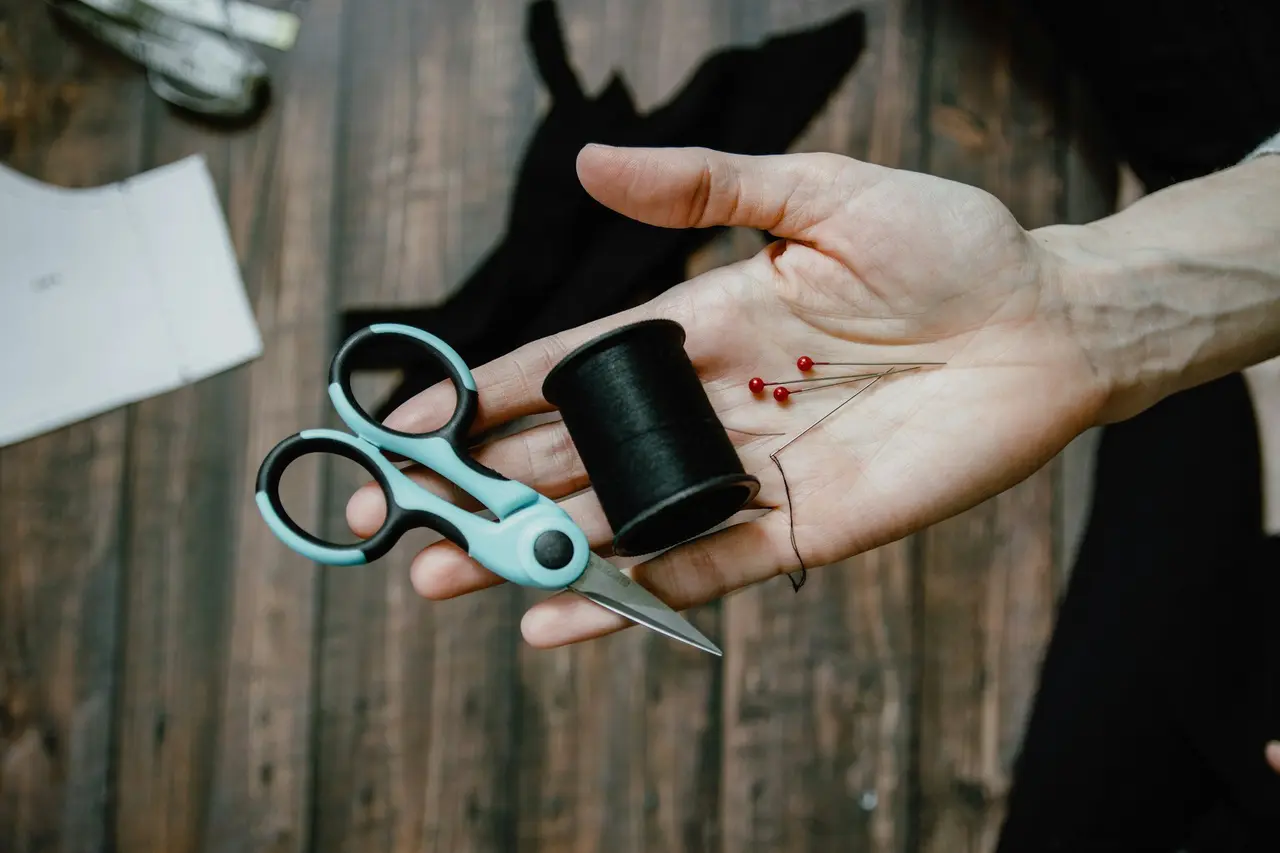 Hands holding scissors and a spool of black thread