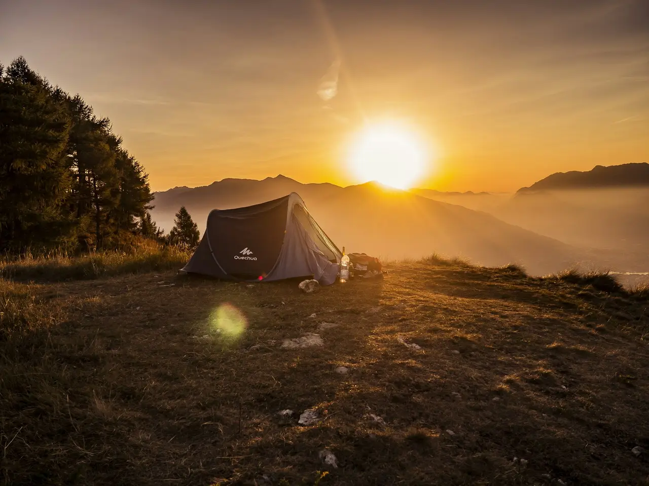 A tent on a mountain top with the sun setting behind it